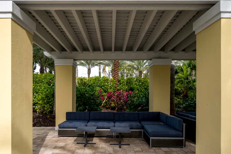 Covered patio with modern sectional seating, yellow walls, and tropical garden view