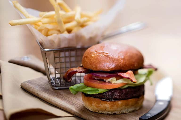 Gourmet burger with bacon and vegetables served with French fries in wire basket