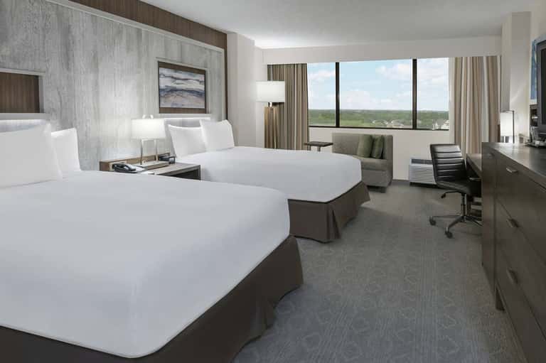 Modern hotel room with two queen beds, floor-to-ceiling windows overlooking landscape, and contemporary furnishings