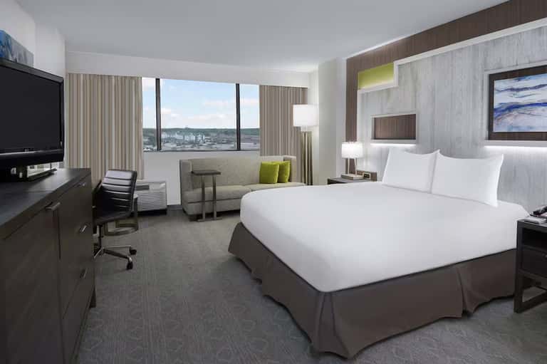 Modern hotel bedroom with bed, workspace, and panoramic city view