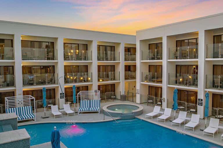 Modern courtyard pool at dusk with striped loungers, spa, and contemporary white building facade