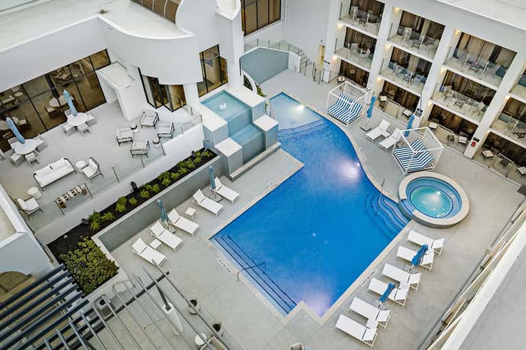 Aerial view of resort pool complex with loungers, spa, surrounding balconied rooms, and landscaping