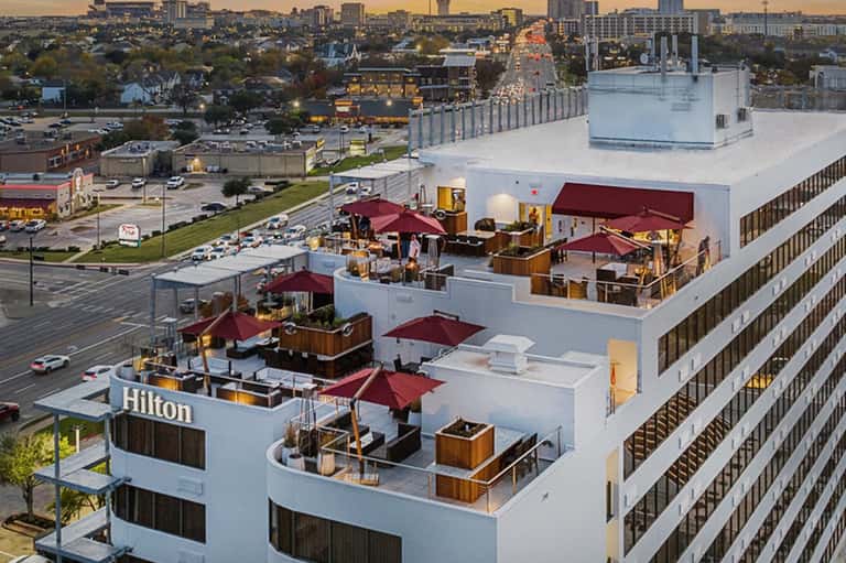 Hilton hotel rooftop with multiple lounge areas, burgundy umbrellas, and city skyline view