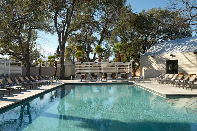 Rectangular resort pool with turquoise water, lounge chairs, and modern poolside buildings with trees