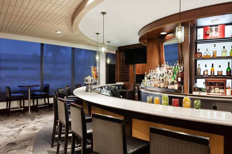 Upscale bar with curved counter, wood paneling, bottle shelves, and ocean view windows