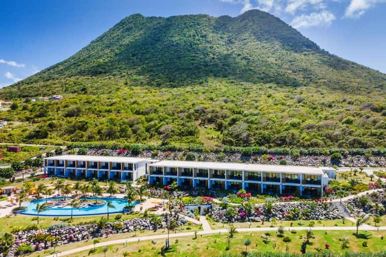 Modern resort building nestled at base of lush green volcano with pool and landscaping