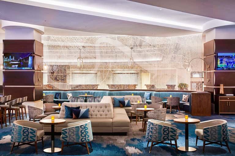 Sophisticated hotel lounge with curved beige sofa, blue accent chairs, warm lighting, and textured wall art