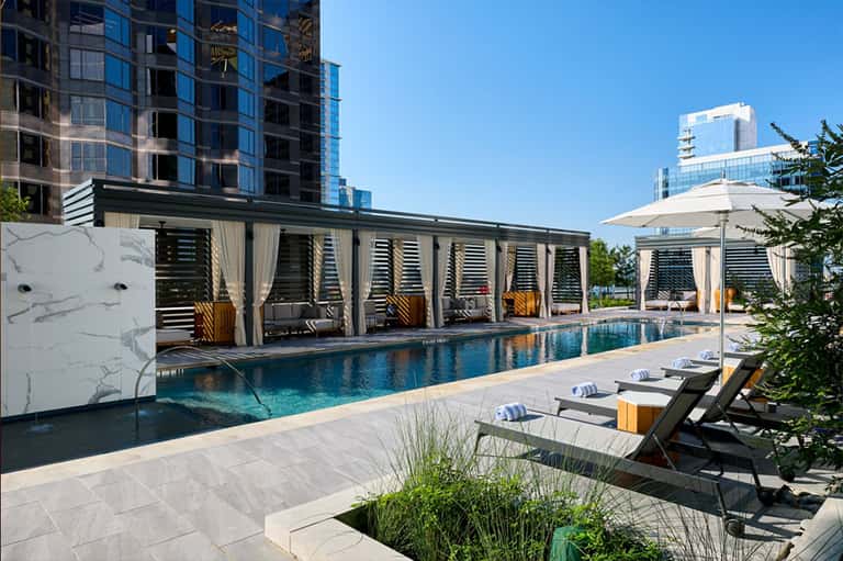 Contemporary rooftop pool with louvered shade structures, modern high-rise buildings, and urban skyline views