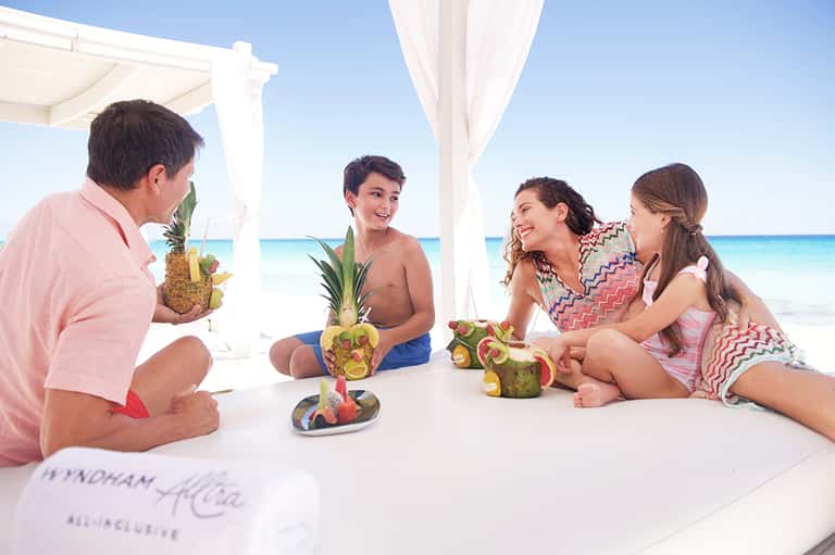 Family enjoying tropical drinks with pineapple garnishes on a beachfront cabana with ocean view