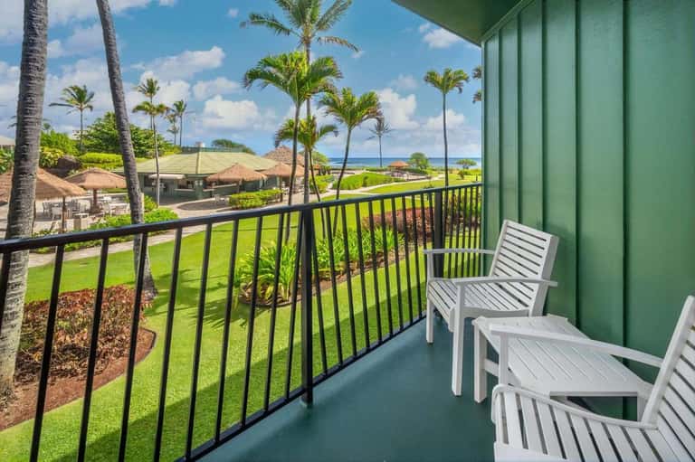 Oceanfront balcony with white Adirondack chairs, palm trees, green lawn, and coastal views