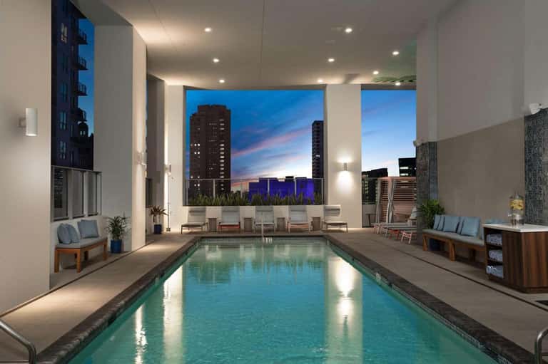Indoor lap pool with city skyline views, modern lighting, and seating areas