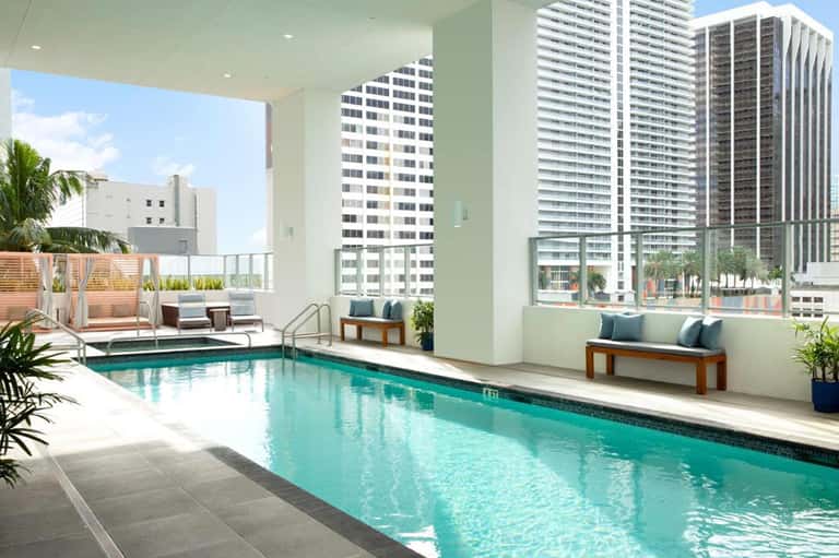 Modern indoor pool on upper floor with city and ocean views, floor-to-ceiling windows, and contemporary seating