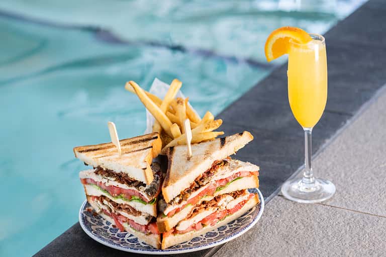 Club sandwich and fries with mimosa cocktail by poolside