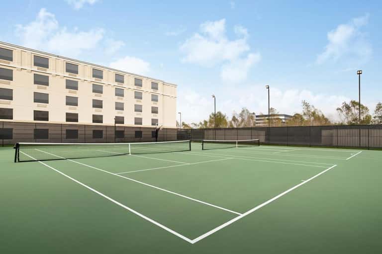 Outdoor tennis courts with green playing surface adjacent to modern hotel building