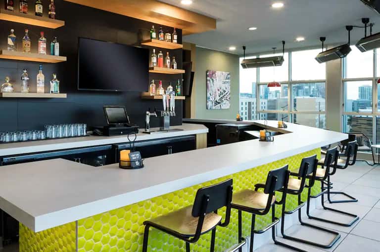 Modern bar lounge with lime green accent panels, black chairs, and panoramic city views