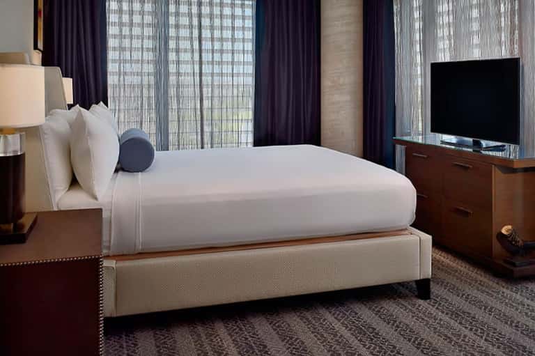 Modern hotel bedroom with king bed, dark curtains, and city view windows