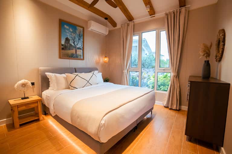 Hotel bedroom with wooden beams, modern furniture, and balcony doors overlooking landscape