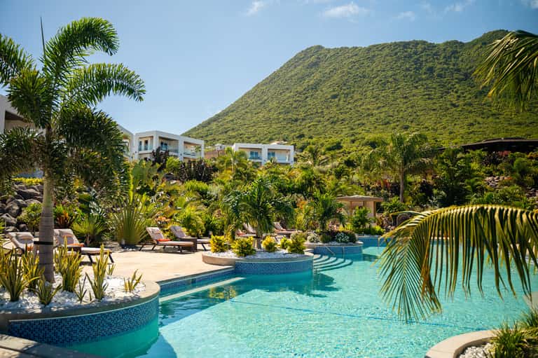Tropical resort pool surrounded by palm trees, lush gardens, and white modern buildings