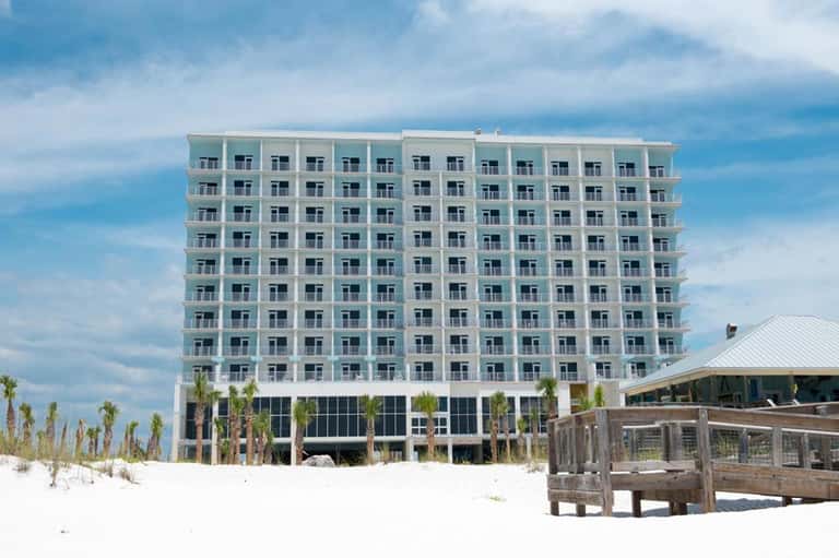 Beachfront hotel building with modern glass exterior, white sand beach and wooden boardwalk entrance