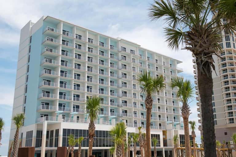 Turquoise and white beachfront resort building with palm trees and balconies