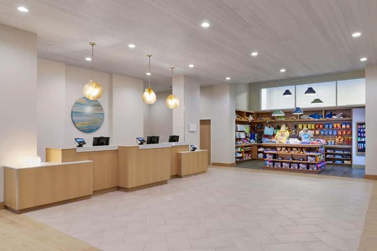 Modern hotel lobby with wooden reception desk, pendant lights, and retail shop with merchandise