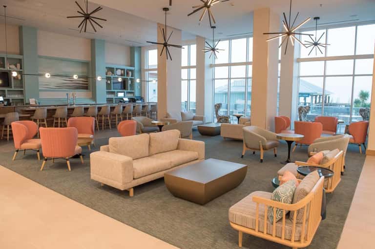 Modern coastal lobby lounge with coral chairs, neutral sofa, starburst lighting, and ocean views