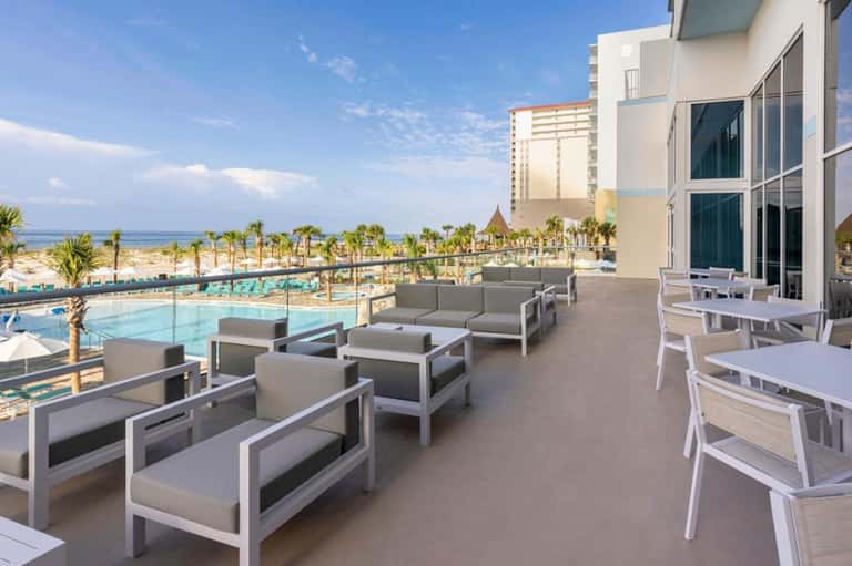 Beachfront terrace with modern lounge seating, pool area, palm trees, and ocean horizon in distance
