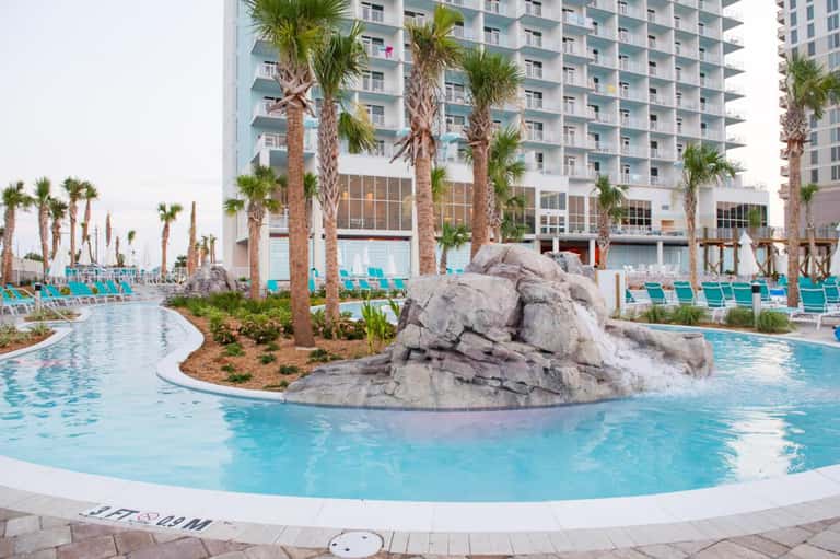 Lazy river pool with rock features, tall palm trees, and high-rise resort buildings in background