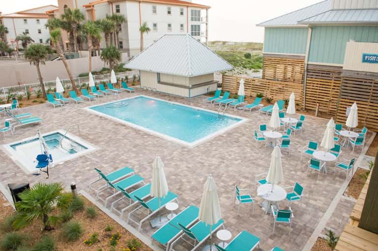 Resort pool area with turquoise lounge chairs, white umbrellas, and beachfront property