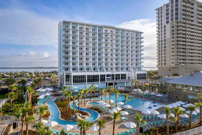 Aerial view of resort with curved pool, high-rise buildings, palm trees, and waterfront