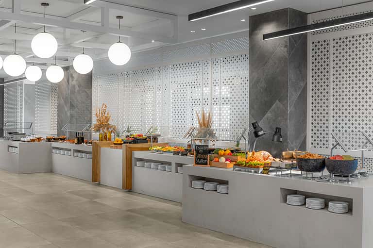 Modern hotel buffet area with white round pendant lights, grey patterned wall panels, and food service stations