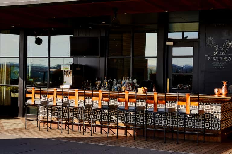 Outdoor bar with orange and black geometric design, mountain views, and modern black building facade