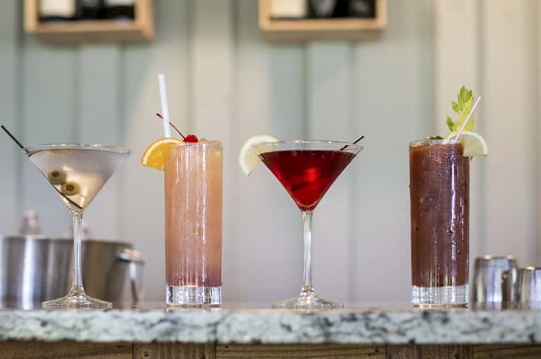 Four craft cocktails on marble bar counter with garnishes and cocktail tools