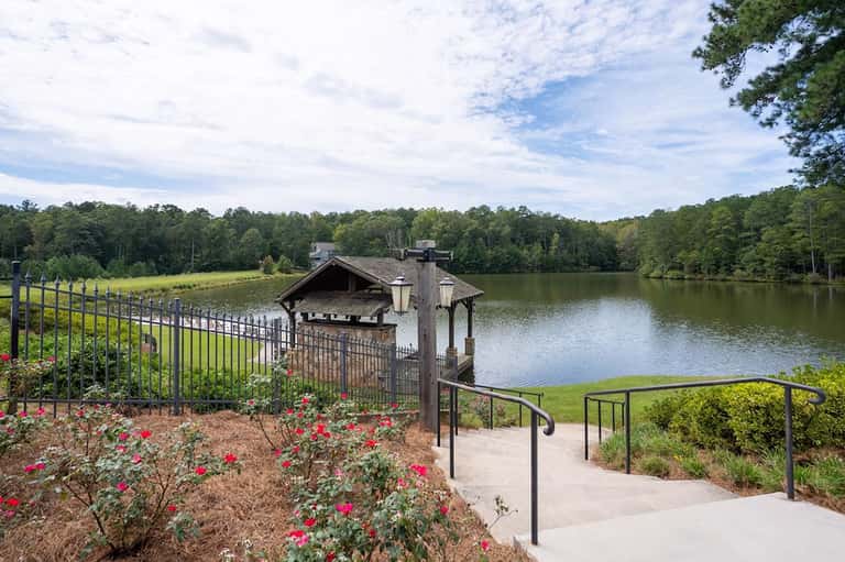 Lakeside gazebo with red flowers, metal railings, and wooden dock structure overlooking calm water