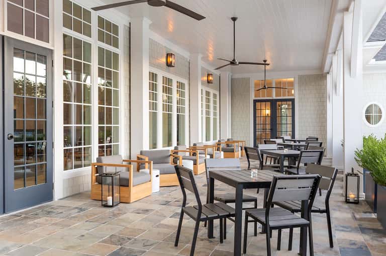 Covered patio with dining tables, wooden lounge chairs, and glass doors overlooking gardens
