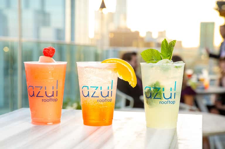 Three colorful cocktails on a rooftop bar with city skyline in the background