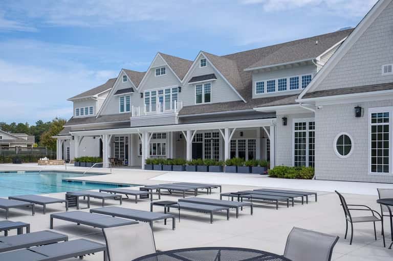 Elegant white coastal house with pool, lounge chairs, and covered patio area overlooking landscaped grounds