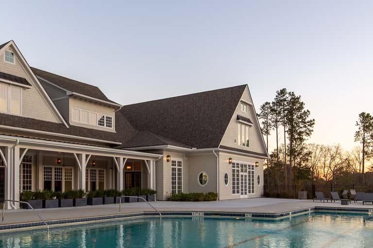 Modern coastal poolhouse with white shingle exterior, large windows, and outdoor swimming pool at dusk
