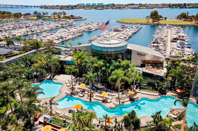 Aerial view of luxury marina resort with multiple pools, palm trees, and hundreds of docked boats in blue water