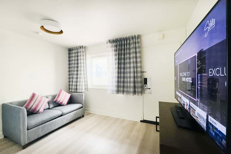 Modern living room with gray sofa, pink striped pillows, checkered curtains, and wall-mounted TV