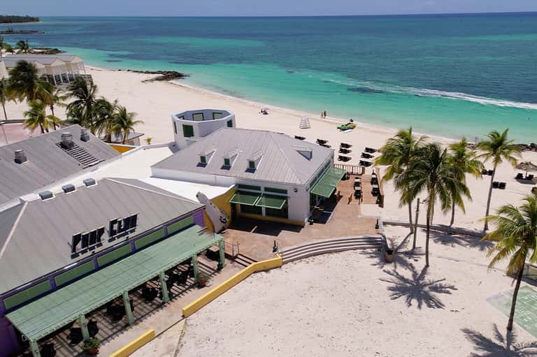 Aerial view of beachfront resort with modern white structures, palm trees, and turquoise ocean waters