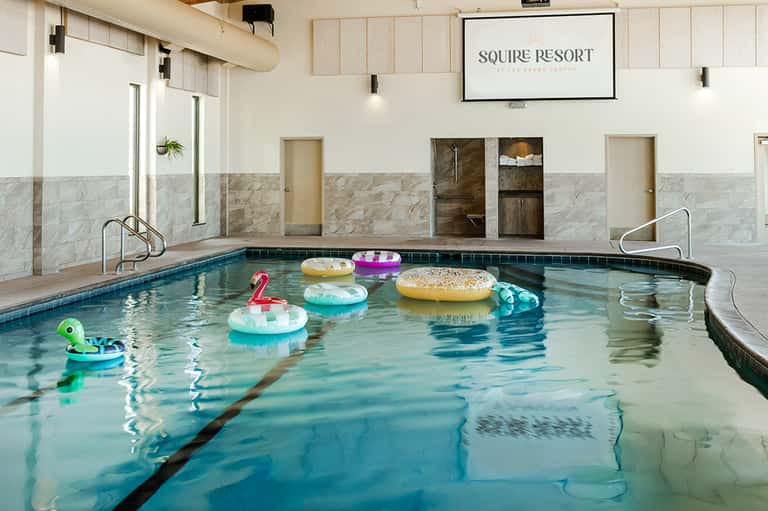 Indoor pool with colorful float toys at Squire Resort, featuring marble walls and lounge chairs