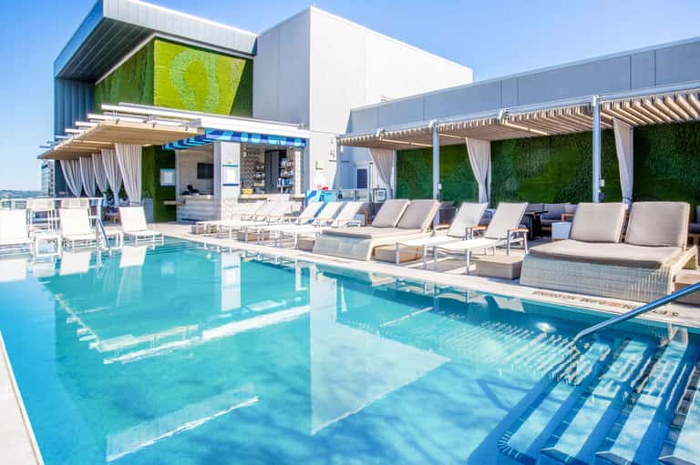 Rooftop pool with turquoise water, white loungers, green living walls, pergolas, and modern architectural features