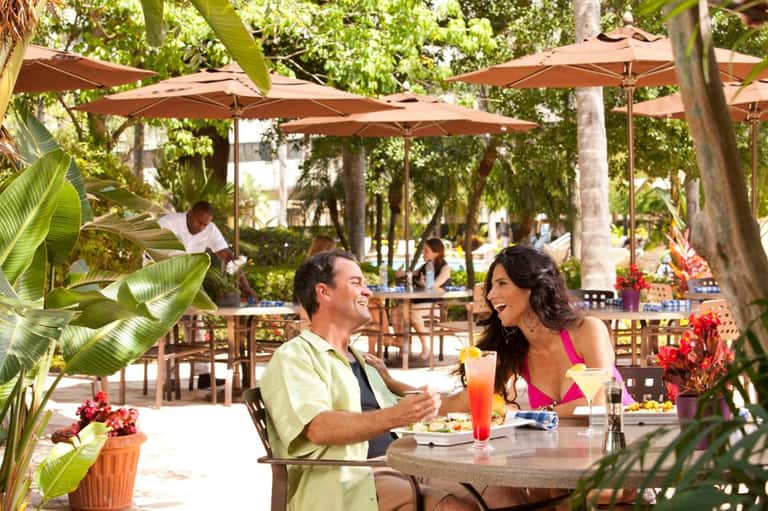 Couple dining outdoors at tropical resort restaurant with umbrellas and lush greenery