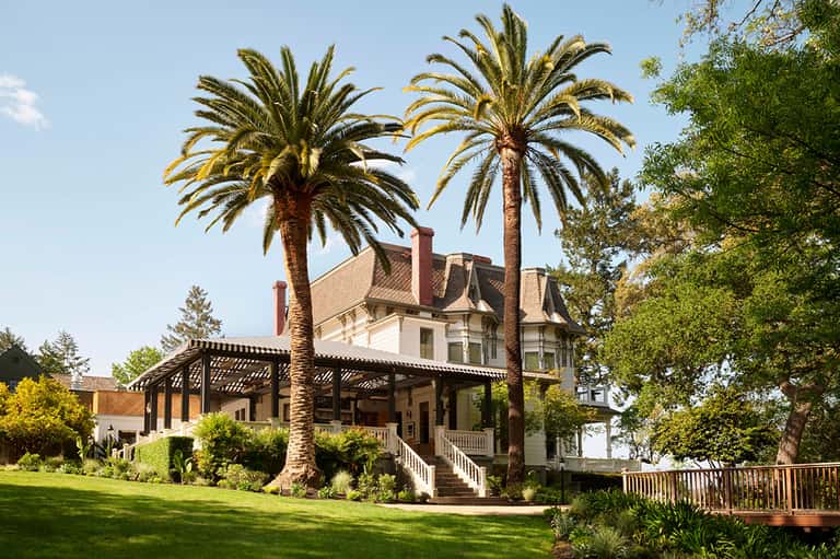 Victorian mansion with palm trees, wraparound porch, and manicured lawn