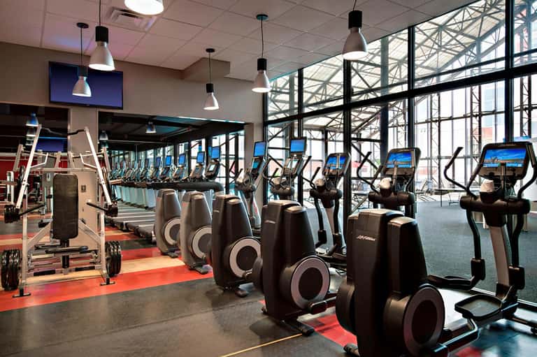Modern fitness center with cardio equipment, weights, and floor-to-ceiling windows overlooking the city
