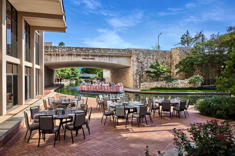 Outdoor dining terrace beside a canal with stone bridges and manicured gardens