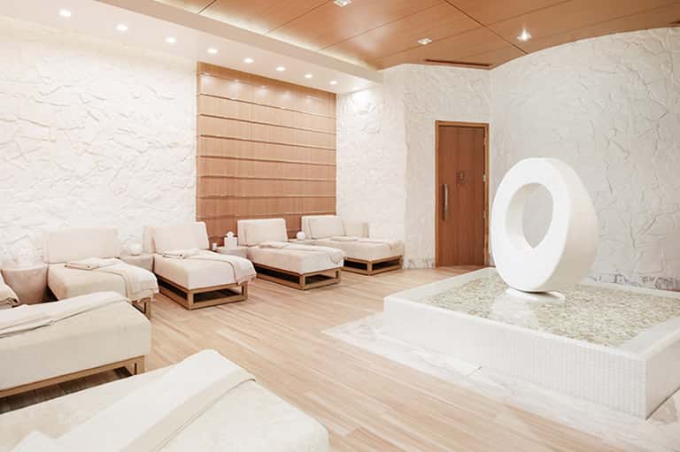 Spa relaxation room with cream loungers, white textured walls, wooden ceiling, and modern white sculptural element