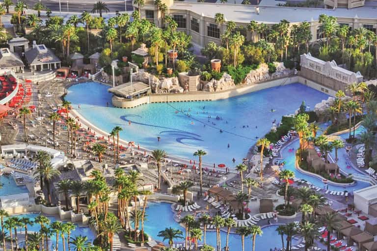 Aerial view of large resort with multiple blue pools, palm trees, and recreational water features