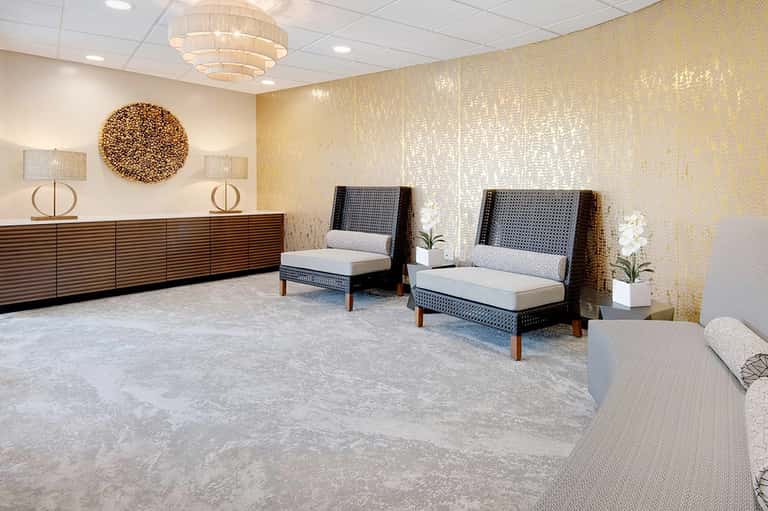 Modern hotel lobby with gold textured walls, wooden reception desk, and contemporary seating areas with neutral upholstery